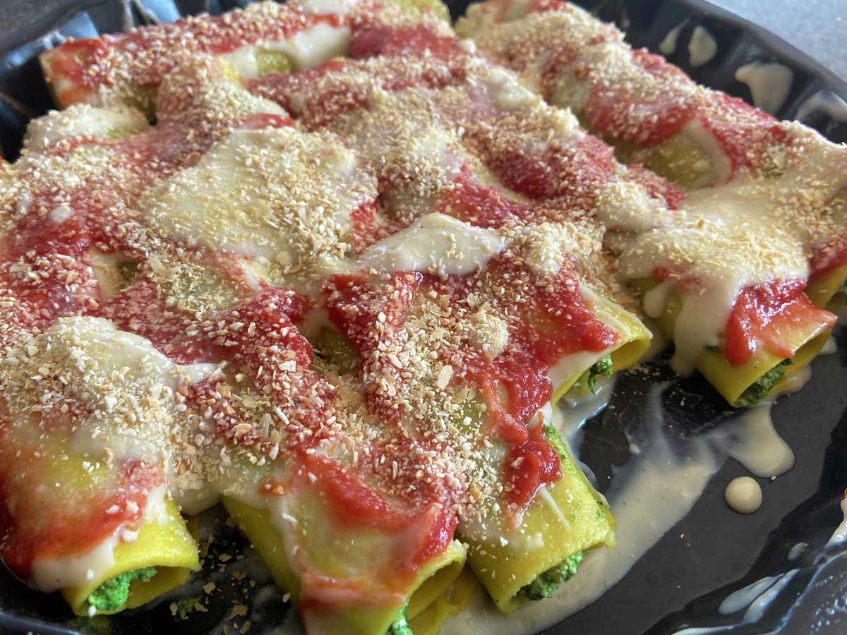 Durante la preparazione: cannelloni vegani ricoperti di pomodoro e besciamella prima di essere infornati