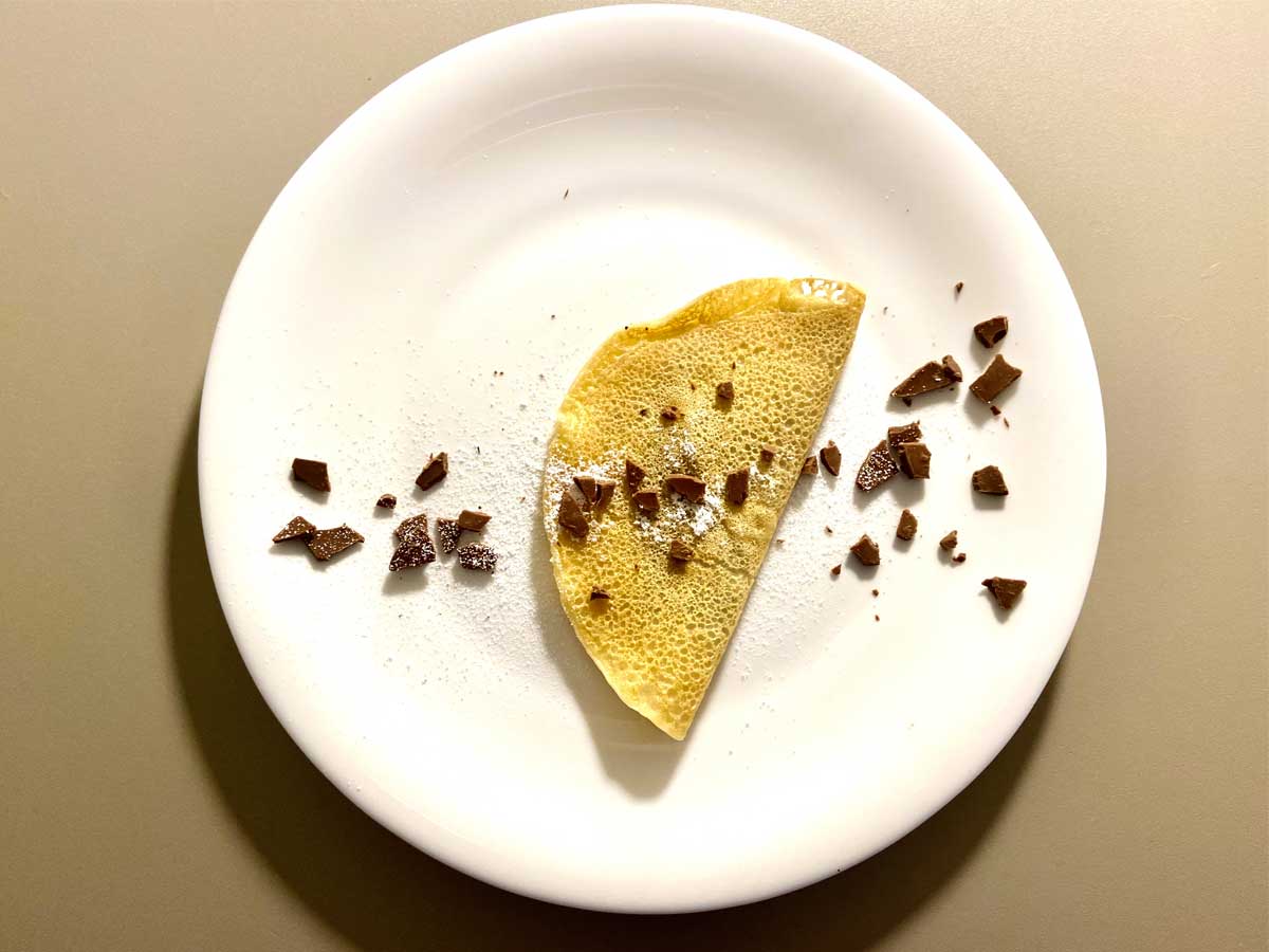 Crepes vegana dolce vista dall'alto su un piatto, con cioccolata e zucchero a velo