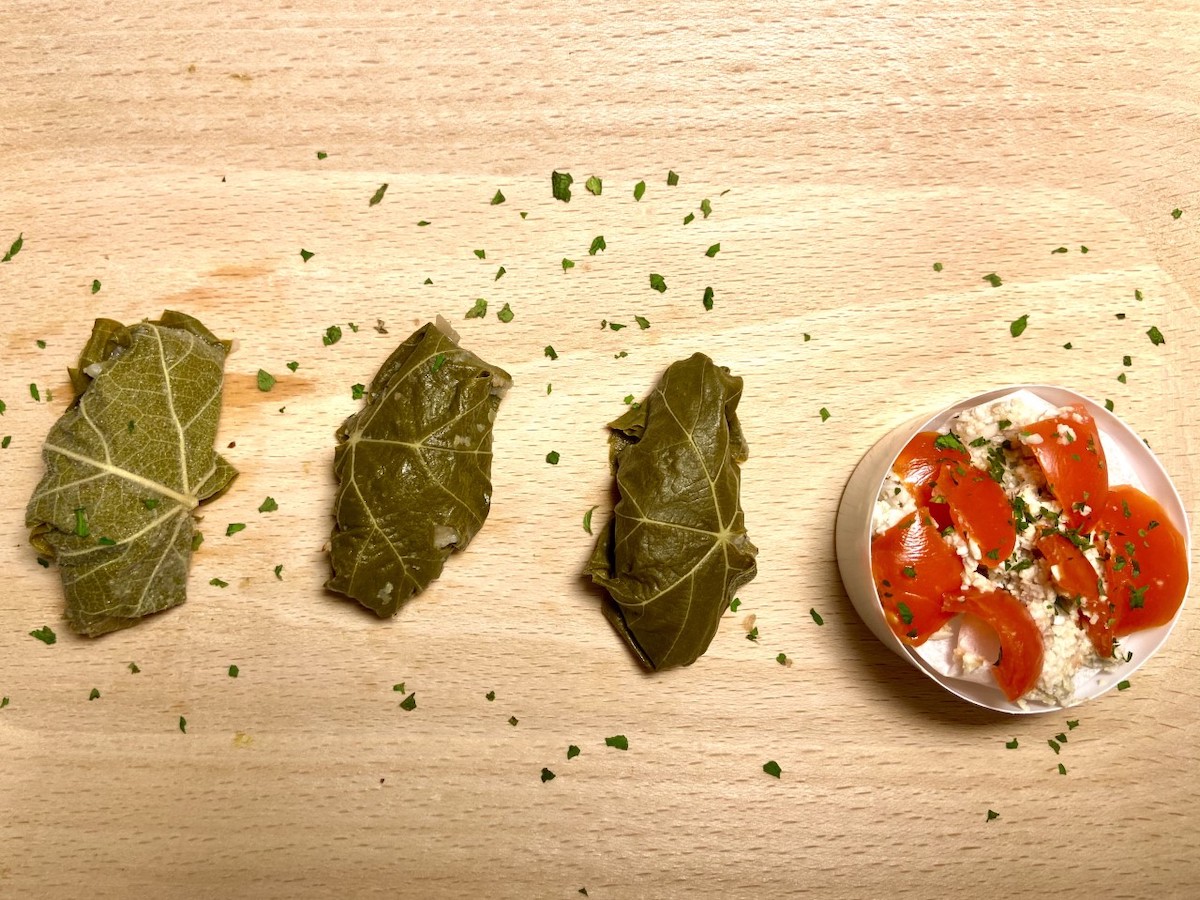 Tagliere con tre involtini di foglie di vite e la salsa vinaigrette viste dall'alto