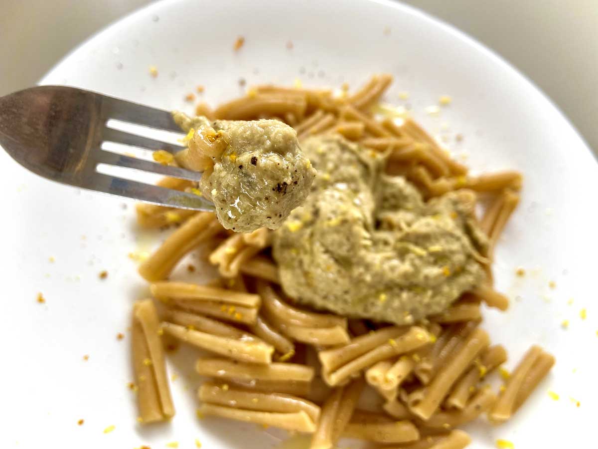 Primissimo piano di una forchetta con la pasta piena di crema ai carciofi e limone