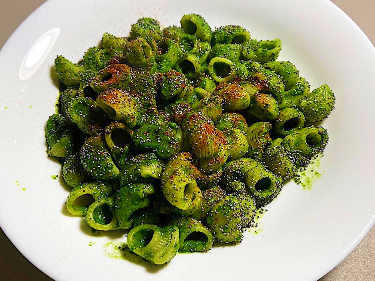 Primissimo piano di un piatto di pasta con spinacini, semi di papavero e paprika