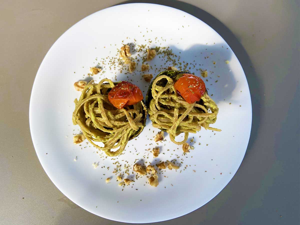 Primo piano di un piatto di linguine con pesto di avocado e limone con pomodorini agrodolci visto dall'alto del piatto