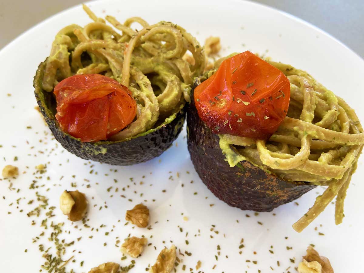 Primissimo piano di un piatto di linguine con pesto di avocado e limone con pomodorini agrodolci visto da tre quarti