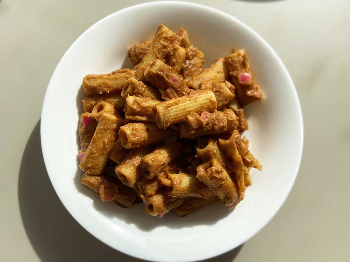 Piatto di rigatoni con passata di lenticchie rosse e cipolle marinate visto dall'alto