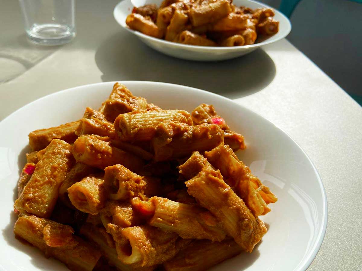 Piatto di rigatoni con passata di lenticchie rosse e cipolle marinate visto da tre quarti