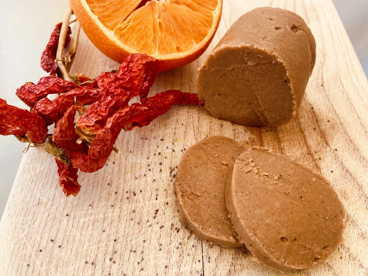 salame vegano affettato su un tagliere con peperoncino e un arancio per decorazione